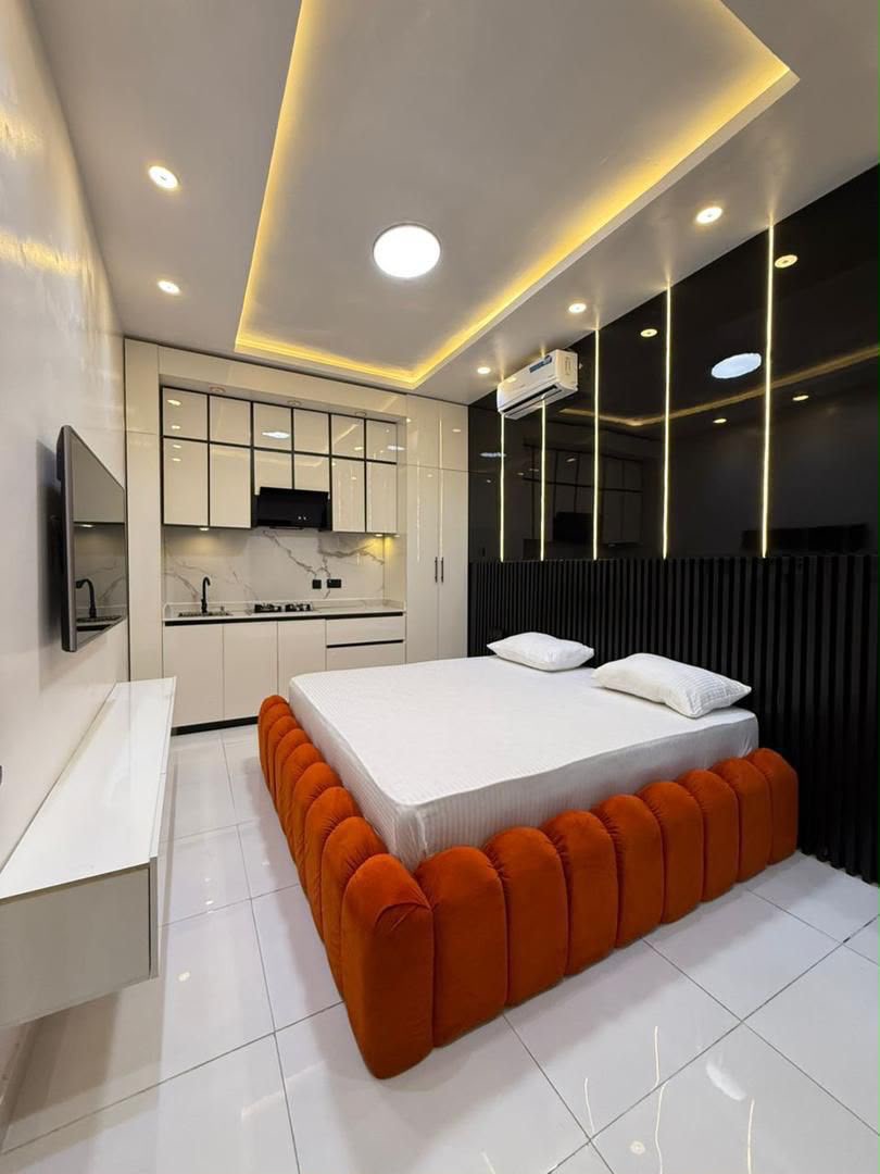 Modern studio bedroom with an orange bed and fitted kitchen